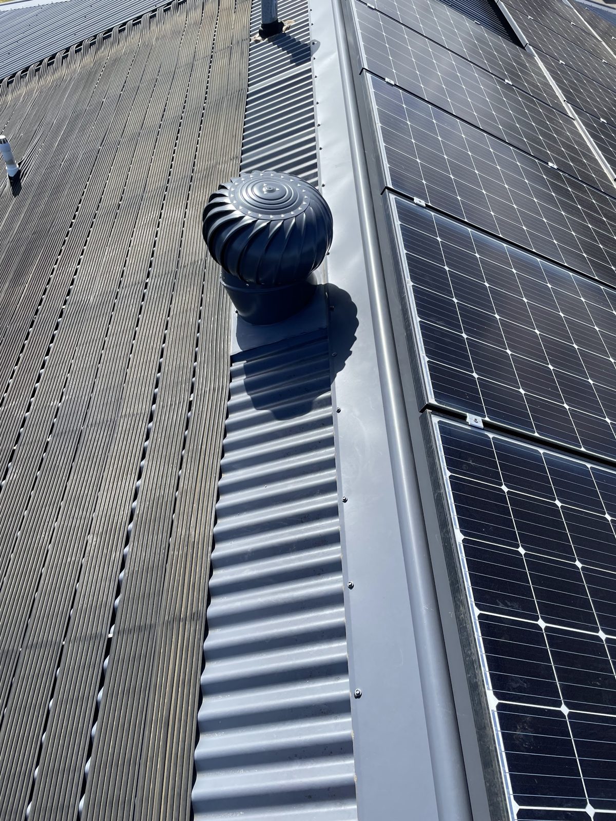 A whirlybird roof vent on a grey metal roof next to rows of solar panels