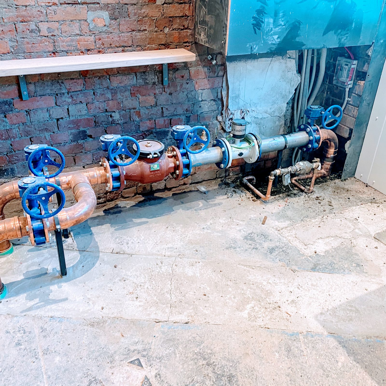 A run of blue-handled valves, copper bends and a meter across an old red brick wall